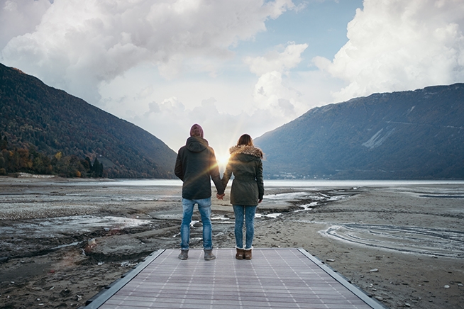 Et ungt par står hånd i hånd og ser utover et fjord